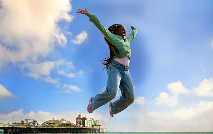 Student jumping in the air on a sunny day, Brighton pier in the background